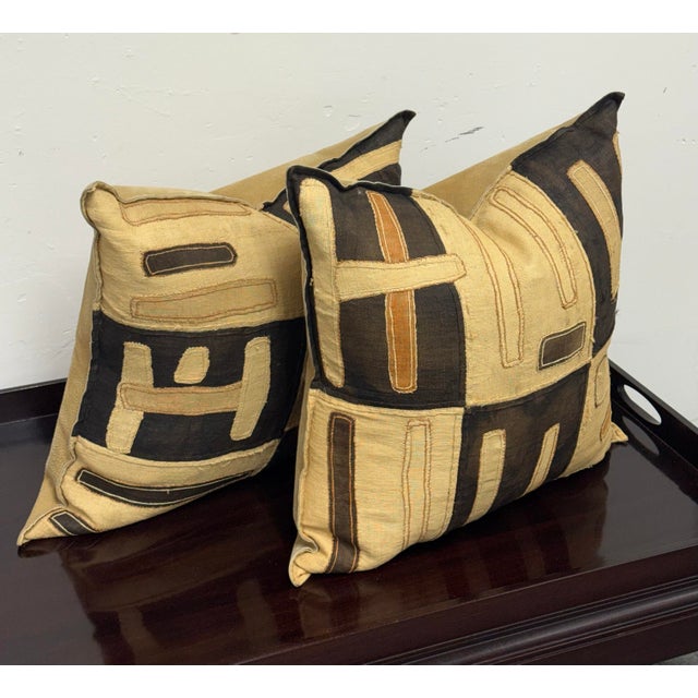Design Plus Gallery presents a Pair of Kuba Cloth Decorative Pillows. Black, tan, and caramel woven textile panels form...
