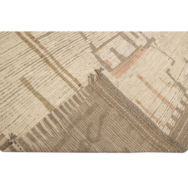 Beautiful Moroccan style handmade wool rug with a beige field. This Modern rug has brown and peach accents featuring a...