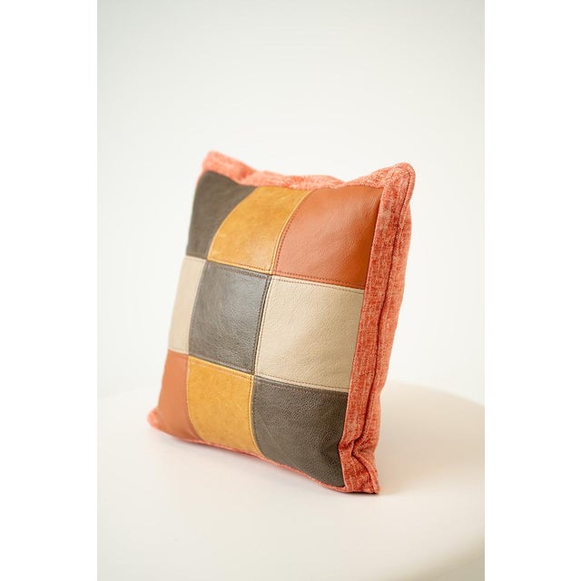 Playful and textural, this square throw pillow showcases a patchwork of orange, tan, and cream leather squares on one...