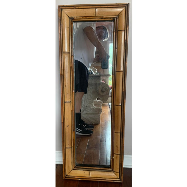 Tall and narrow wall mirror made of a wood frame with bamboo veneer surrounding the glass.