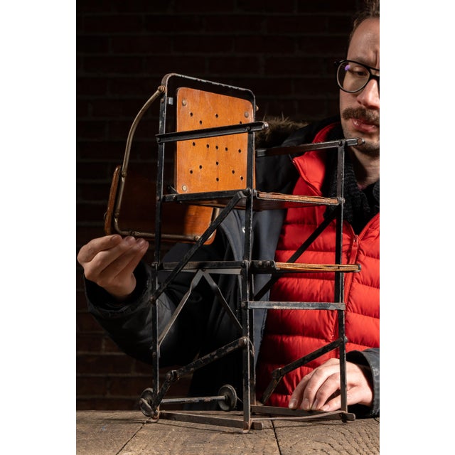 Compact wood-and-metal folding highchair constructed to demonstrate a collapsible, accordion-style mechanism. The chair...