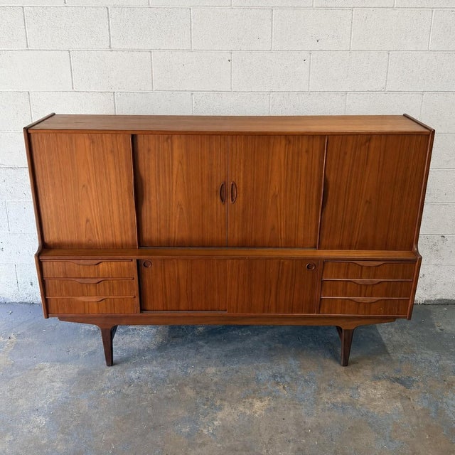 A large vintage Danish teak highboard dating to the 1960s, designed with generous storage across two levels and a warm,...
