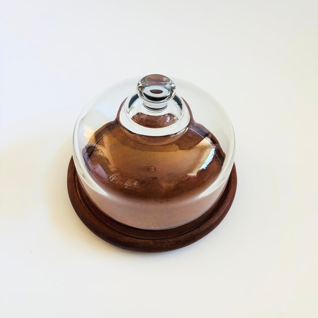 A vintage glass cloche. The top is made of heavy glass with an integrally formed handle sitting on a circular teak base. A...