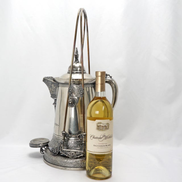 A large silver-plated water tipper that has Aesthetic Movement artistry with owls, herons, butterflies, fans, and flowers...