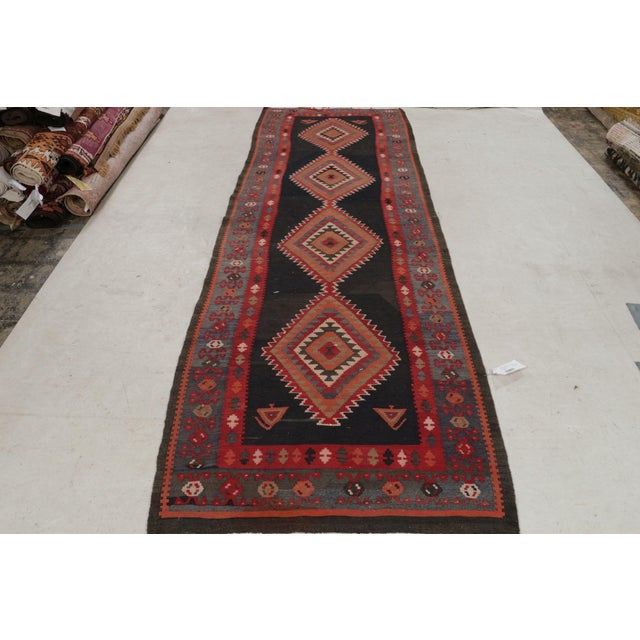 Handwoven in wool circa 1920-1930, this 4×12 antique Perisna Kilim connotes a Kermanshad rug design, exemplifying bold...
