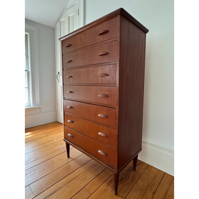 A striking Danish Modern chest of drawers in rich teak, featuring seven graduated drawers with sculpted half-moon pulls —...