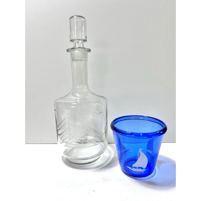 A vintage nautical barware pairing featuring a clear glass decanter etched with a detailed sailing ship and a cobalt-blue...
