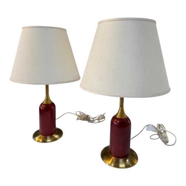 Elegant pair of vintage table lamps featuring deep red cylindrical bases with polished brass accents and wide cream linen...