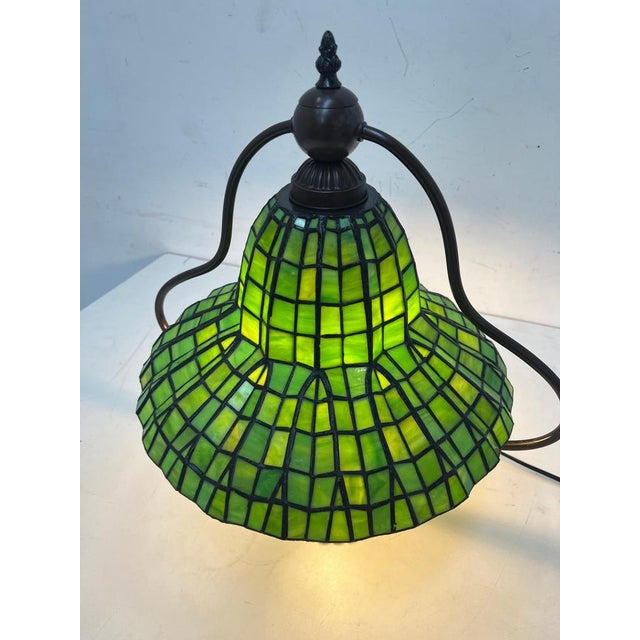 Elegant Tiffany-style table lamp featuring a beautifully crafted green stained glass shade with geometric patterning. The...