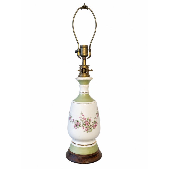 A charming vintage ceramic table lamp featuring a graceful urn-shaped silhouette, delicate floral decoration, and soft...