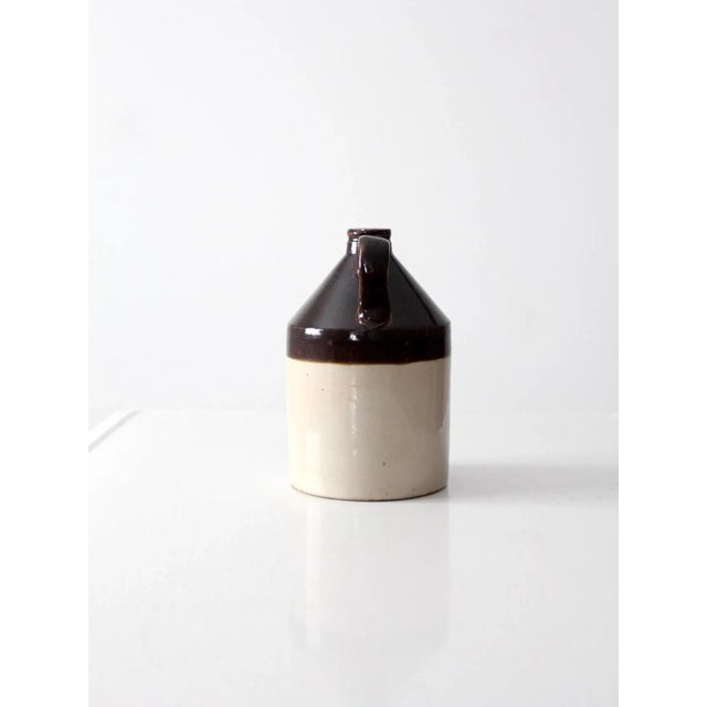 An antique stoneware crock jug featuring a rich brown Albany slip glaze with a warm, understated finish. The traditional...