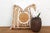 A dense arrangement of gold-tan motifs covers nearly the full face of this pillow — a sun-disc medallion at center, framed...