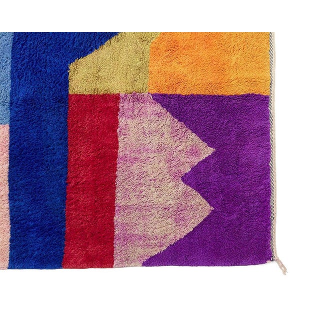 This oversized hand-knotted wool rug features a bold abstract geometric composition rendered in a vibrant spectrum of ruby...