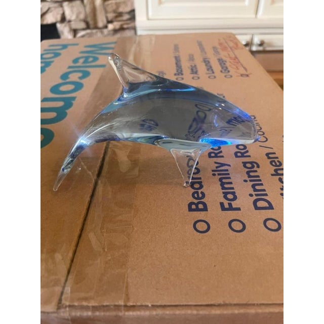 This is a sleek, blue-tinted art glass sculpture shaped like a jumping dolphin. It is crafted with a transparent finish...