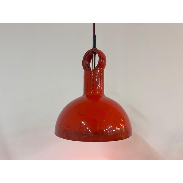Large dining table lamp made of glossy, lacquered ceramic in a vibrant red. The wide shade provides a pleasant, downward-...