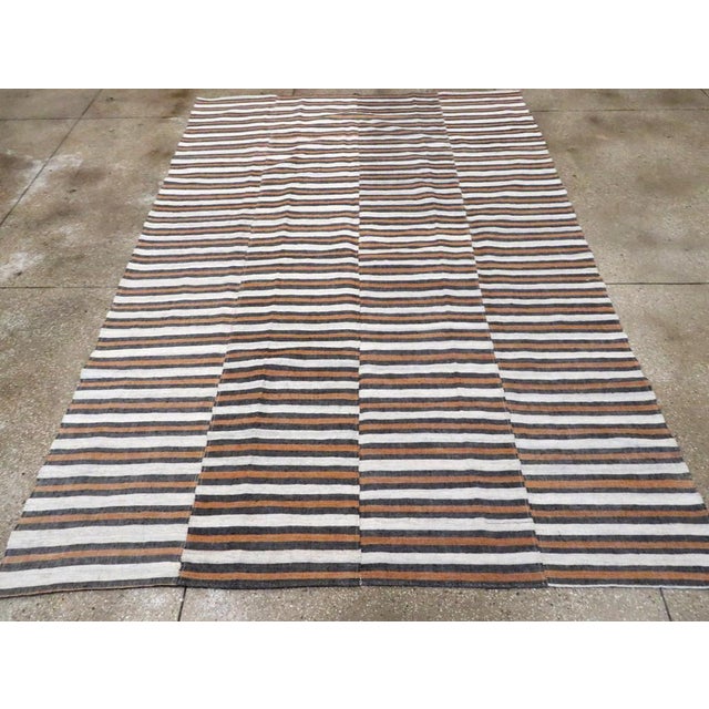 This mid-20th century Turkish flatweave kilim rug, features a lively horizontal stripe design arranged across three...