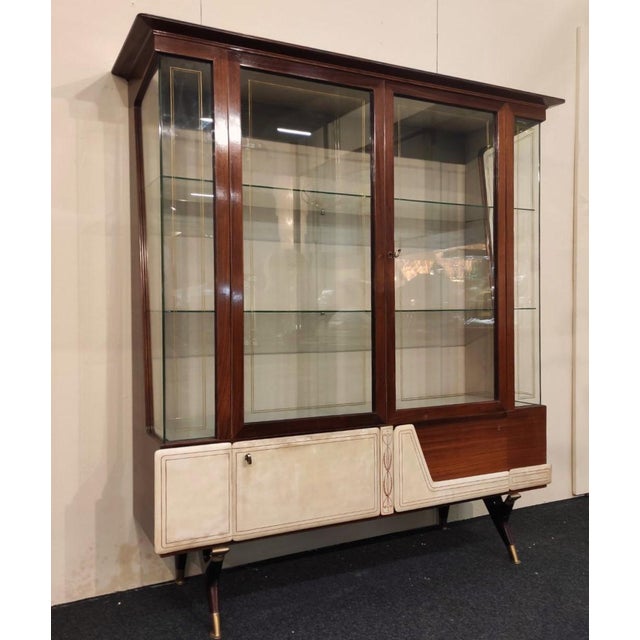 A refined display cabinet, featuring angled glass panels that lend the entire cabinet a luminous ambience. The wooden...