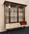 A refined display cabinet, featuring angled glass panels that lend the entire cabinet a luminous ambience. The wooden...