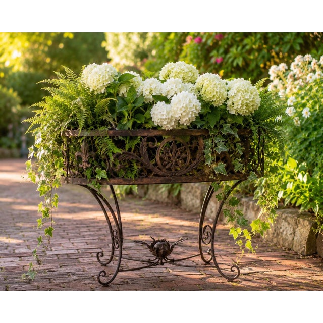 Charming vintage wrought iron jardinière stand featuring twisted iron supports, decorative fleur-de-lis motifs, and an...