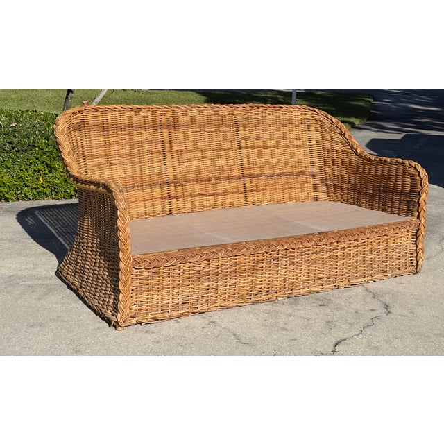 A striking vintage woven rattan lounge sofa featuring a dramatic curved silhouette and oversized braided trim. Its...