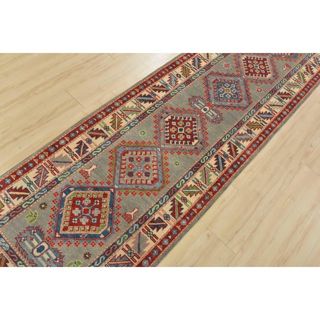 A tribal Caucasian Kazak runner hand-knotted with fine wool on a cotton foundation. This rug features a row of geometric...