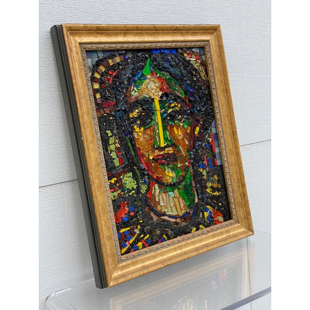 Framed mosaic portrait of a woman, done primarily with bits of colored glass adhered to a wood back, the edges sheathed in...
