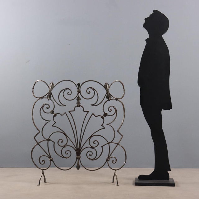 Arched wrought iron fireplace guard supported by four legs. Decorated with curls and scrolls. This piece is attributed to...