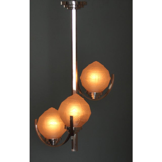 This Art Deco chandelier is chrome-plated and features three glass globes with Art Deco ornaments, offset in height. A...