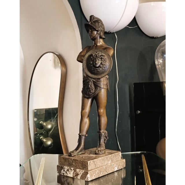An elegant tabletop sculpture in burnished bronze depicting the mythological hero Perseus, portrayed in a proud and...