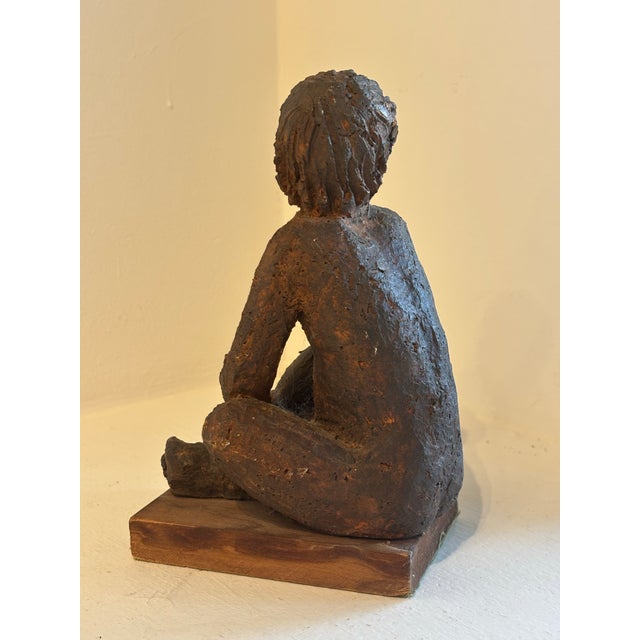 Seated ceramic figure of young boy on wooden stand. Could be used as a paper weight or a bookend, or as an accent piece.