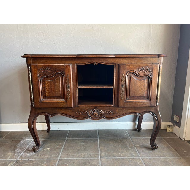 This vintage Belgian oak sideboard features exquisite floral carvings, brass barrel hinges, and classic cabriole legs....
