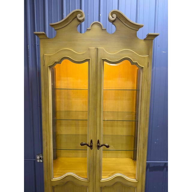 Tall vintage French Provincial style display cabinet featuring a light painted finish, decorative shaped crown, glass...