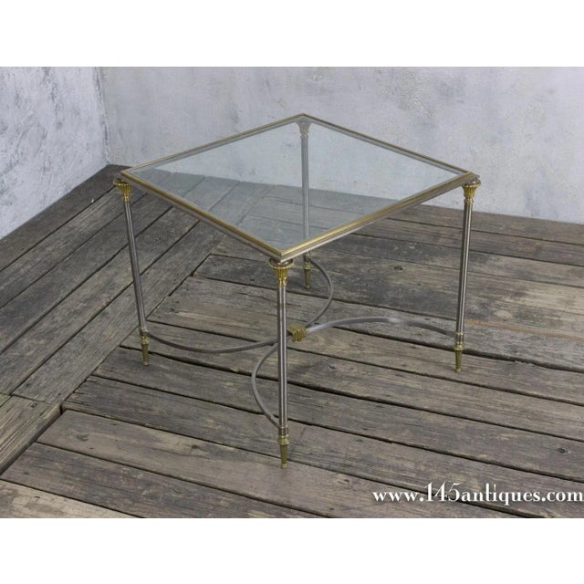 This square polished steel coffee table features brass highlights, a center stretcher, and an inset glass top. Reminiscent...