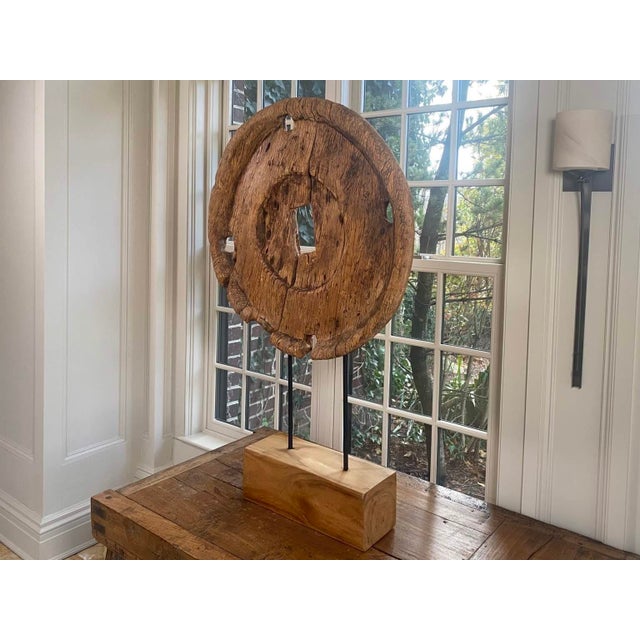 A large circular teak Indonesian Ox cart wheel sculpture with rectangular cut outs to center and outer edge on a custom...