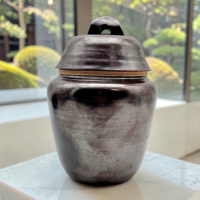 A hand-thrown Japanese studio pottery tea storage jar finished in a rich tenmoku glaze that deepens from warm iron brown...