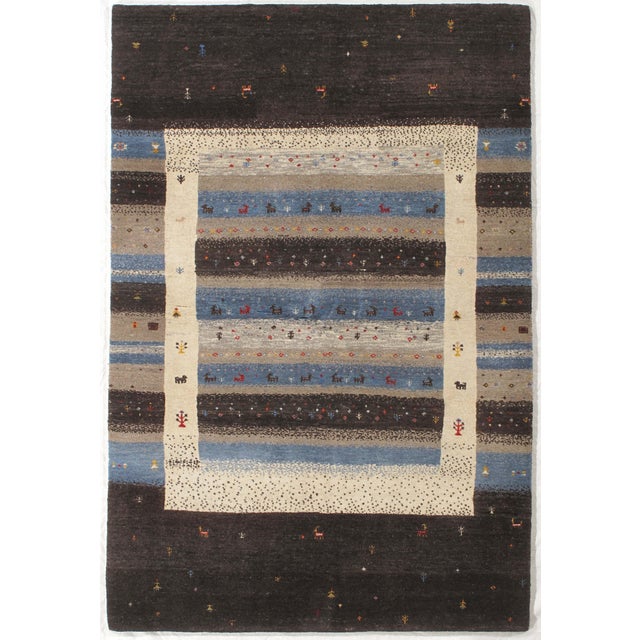 Hand-knotted Indo Gabbeh wool rug featuring layered horizontal bands in blue, gray, and ivory tones with small stylized...