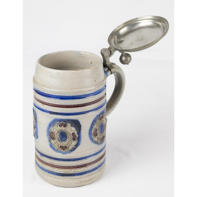 Beautiful glazed ceramic mug with blue decorations and red hearts and pewter lid. Origin Germany. Under the lid is...