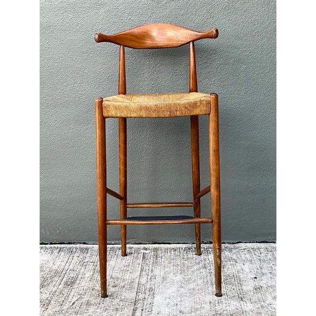 This vintage Mid-Century Modern bar stool is defined by its sculptural, horn-shaped backrest, a single carved wood crest...