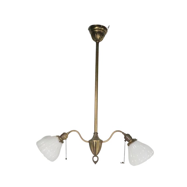 Classic early electric brass two light chandelier, white period milk glass bell shades. The light fixture features a...