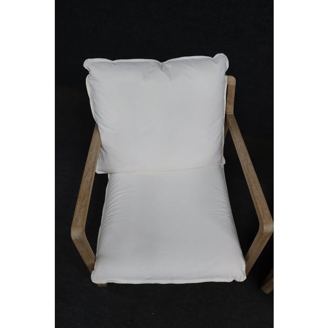Pair of sling lounge chairs featuring angular washed oak frames with low-profile silhouettes and relaxed white linen-style...