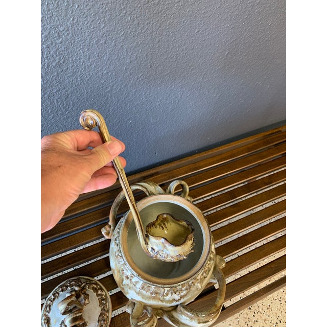 Ornately sculpted stoneware tureen with a drip glaze in warm earth tones. The ladle has the look of melting metal. This is...