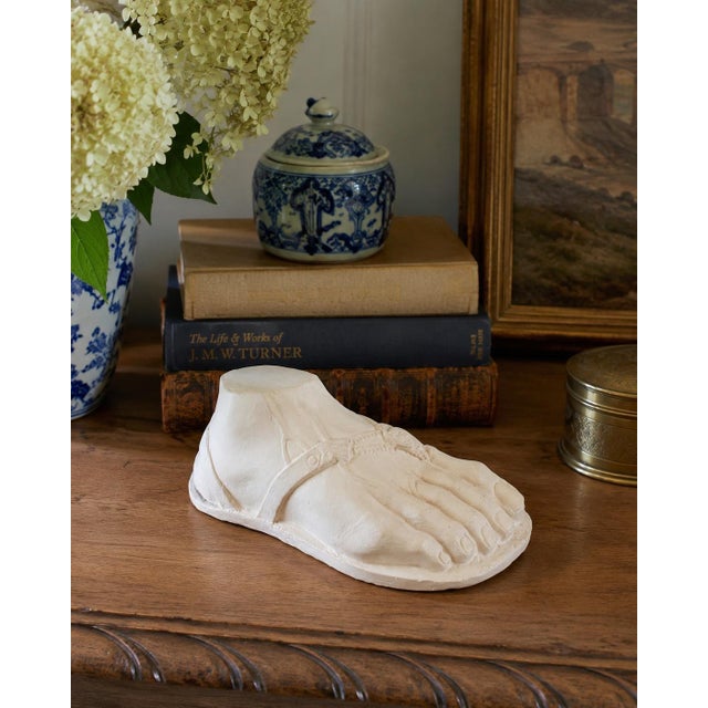 A striking Grand Tour-style plaster sculpture depicting a sandaled foot inspired by classical Greek and Roman antiquity....