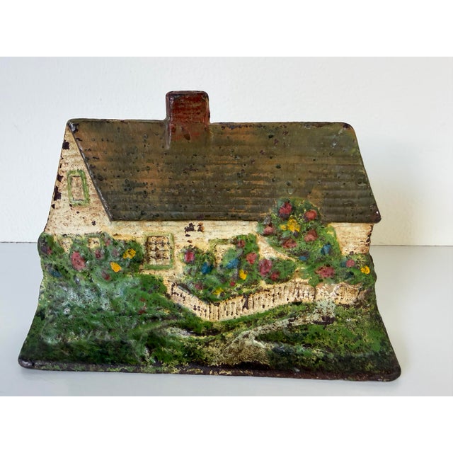 Charming vintage cast iron doorstop crafted in the form of a quaint countryside cottage, featuring a hand-painted garden...