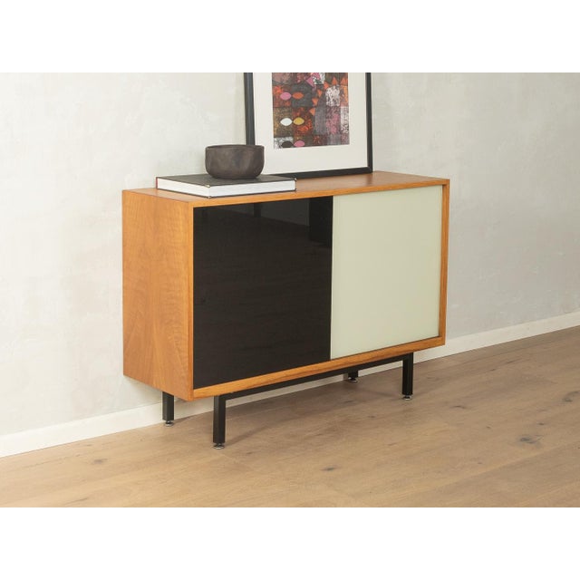 Classic chest of drawers from the 1950s. Walnut veneer body with two black and cream-white glass sliding doors, one shelf,...