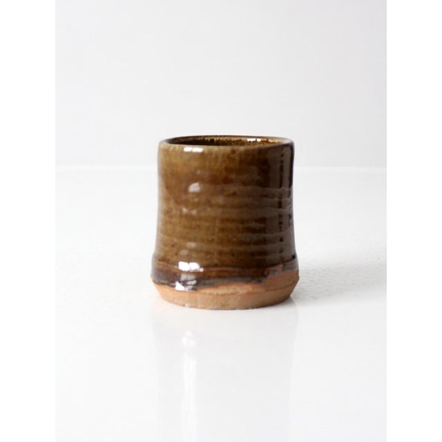 Vintage handmade studio pottery cup in a rich brown glazed finish with subtle tonal variation and an unglazed foot. The...