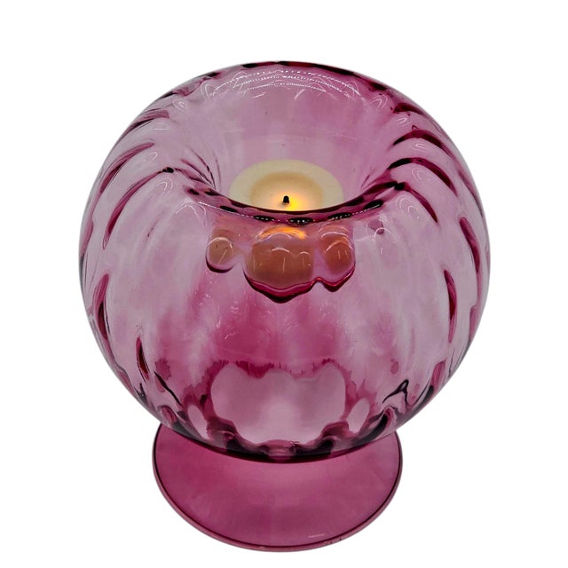 Glass drawn from flame, plum-hued and luminous, shaped in optic ripples that catch and scatter light. Its form, inverted...