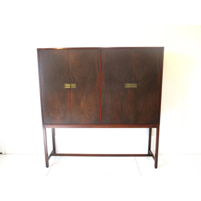 A sophisticated two-piece four door nicely burled mahogany cabinet / server with brass pulls sitting on a lower frame....