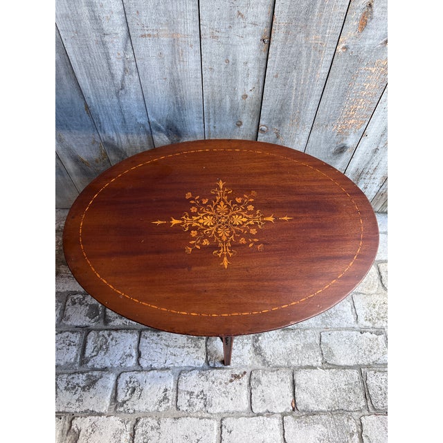 A charming antique oval side table crafted in mahogany, featuring an exquisite hand-inlaid satinwood floral marquetry...
