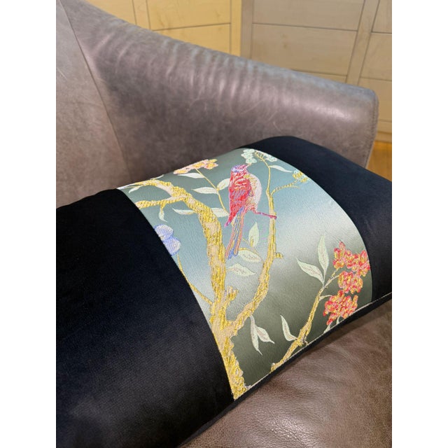A lumbar cushion cover with a celadon satin jacquard center strip showing a red songbird perched on a gold branch,...