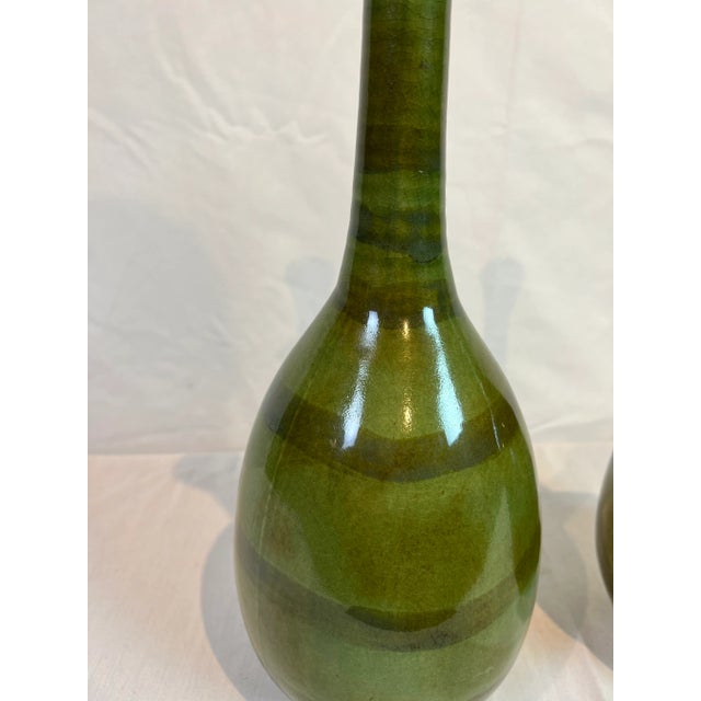 Green vase featuring a crackle glaze and aged green finish with long neck. Hand made items may vary in size, pattern and...